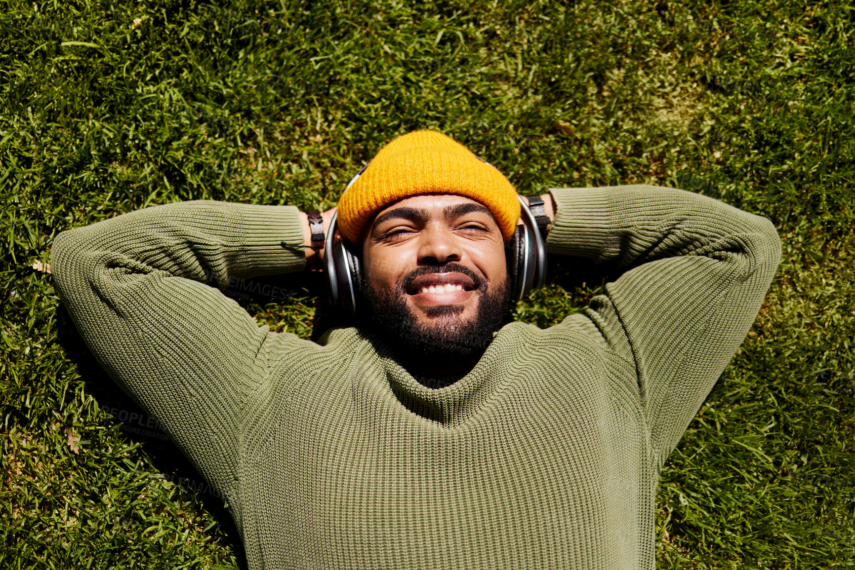 Buy stock photo Relax, music headphones and happy man on grass outdoor, listen to audio online or hearing sound of podcast from top view. Smile, streaming radio and person at park resting for peace, calm and freedom