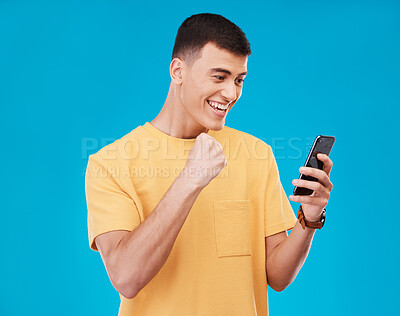 Buy stock photo Phone, celebration and young man in a studio with fist pump for winning, success or achievement. Happy, smile and male winner from Canada cheering for prize on cellphone isolated by blue background.