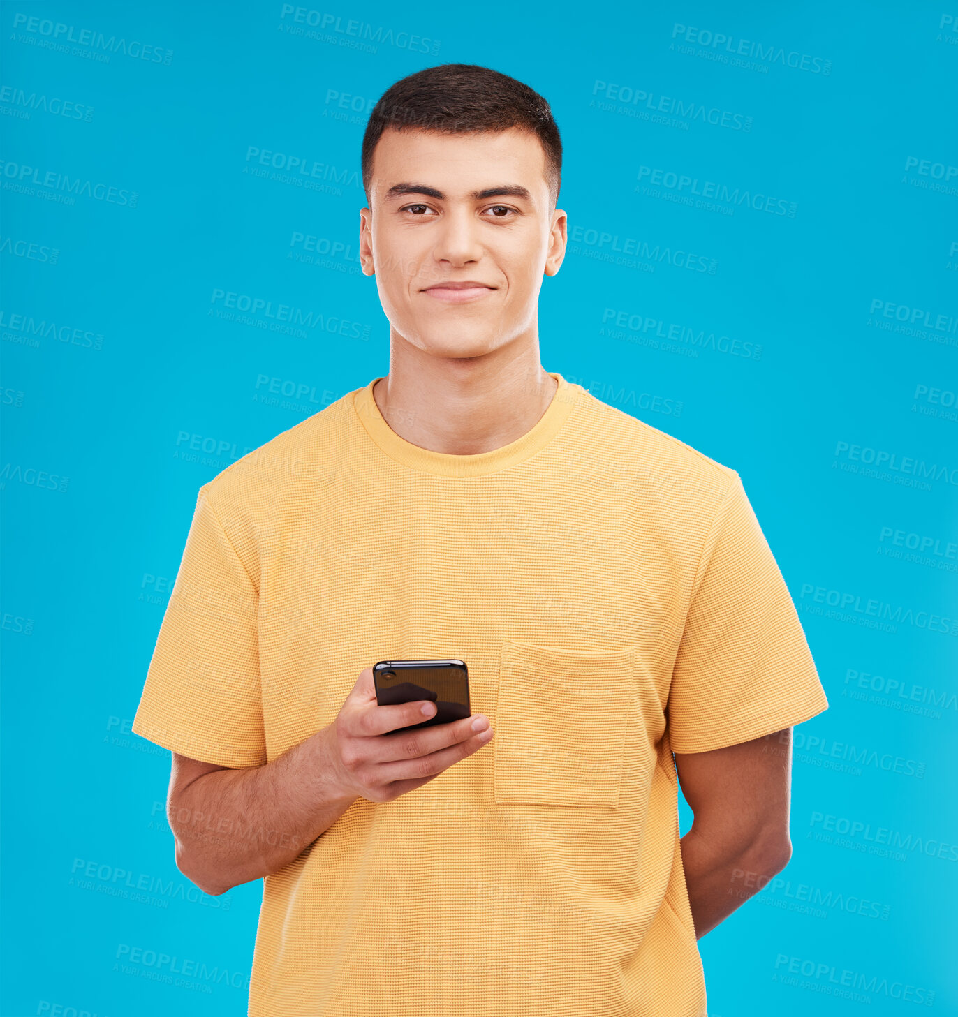 Buy stock photo Phone, portrait and young man in studio networking on social media, mobile app or internet. Smile, technology and male person from Canada scroll on website with cellphone isolated by blue background.
