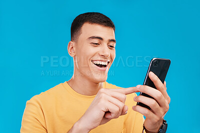 Buy stock photo Phone, excited and young man in a studio scroll on social media, mobile app or the internet. Smile, happy and male person from Canada networking on website with cellphone isolated by blue background.