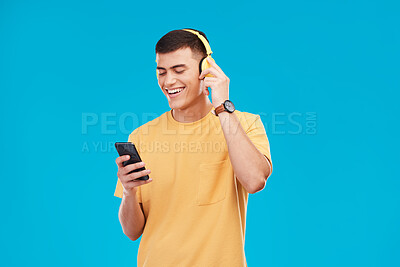 Buy stock photo Phone headphones and young man in a studio listening to music, radio or playlist for entertainment. Smile, technology and male person streaming a song, podcast or album isolated by blue background.