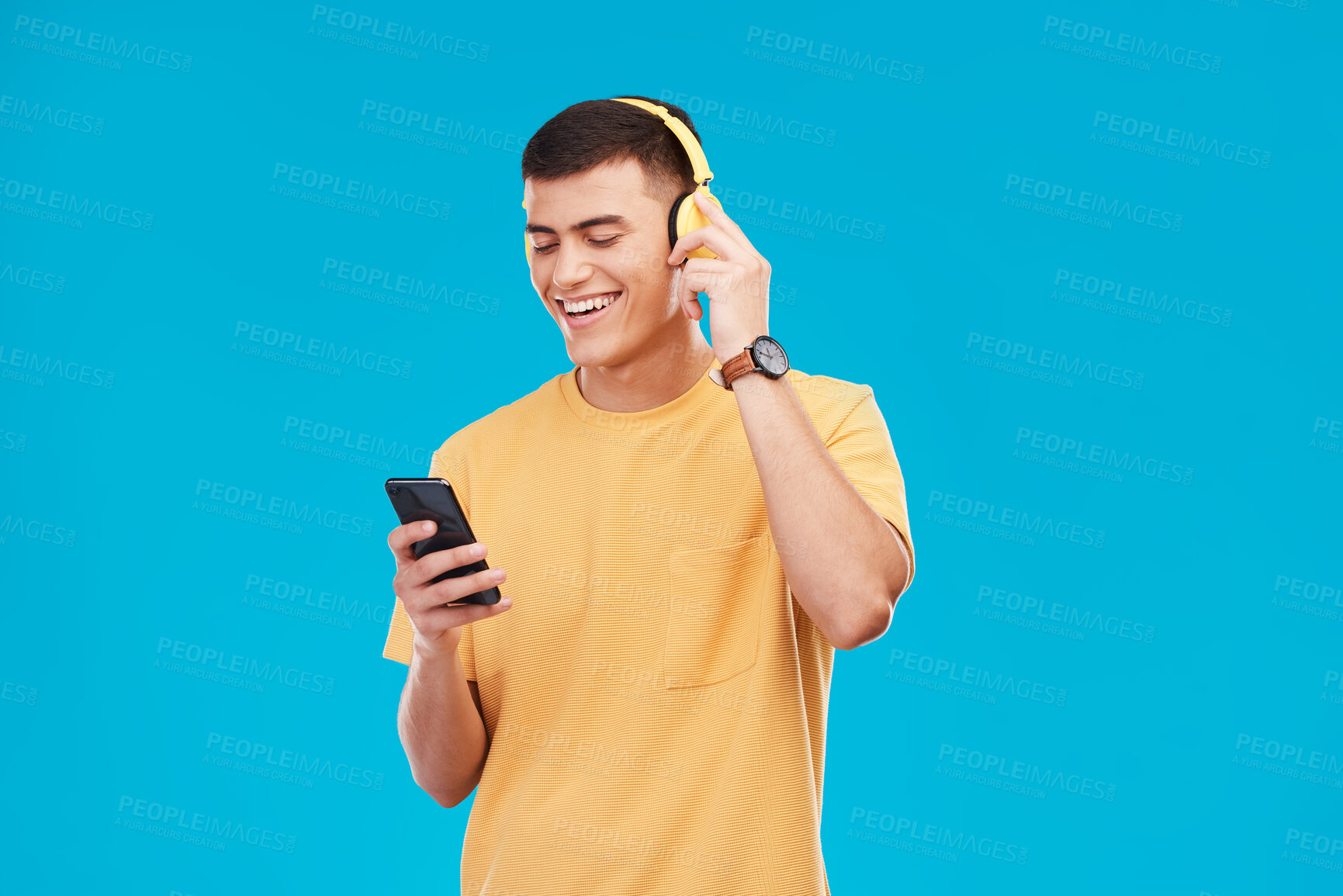 Buy stock photo Phone headphones and young man in a studio listening to music, radio or playlist for entertainment. Smile, technology and male person streaming a song, podcast or album isolated by blue background.