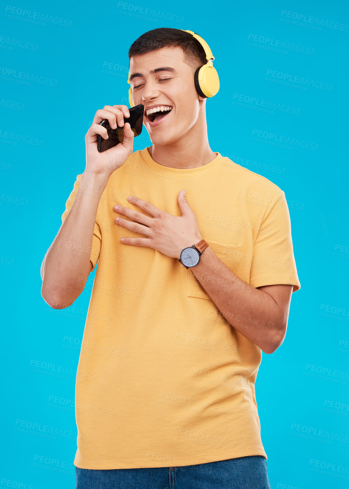 Buy stock photo Man, headphones and singing to music with smartphone, listening to radio with karaoke on blue background. Fun, playful and entertainment with technology, audio streaming and using phone app in studio