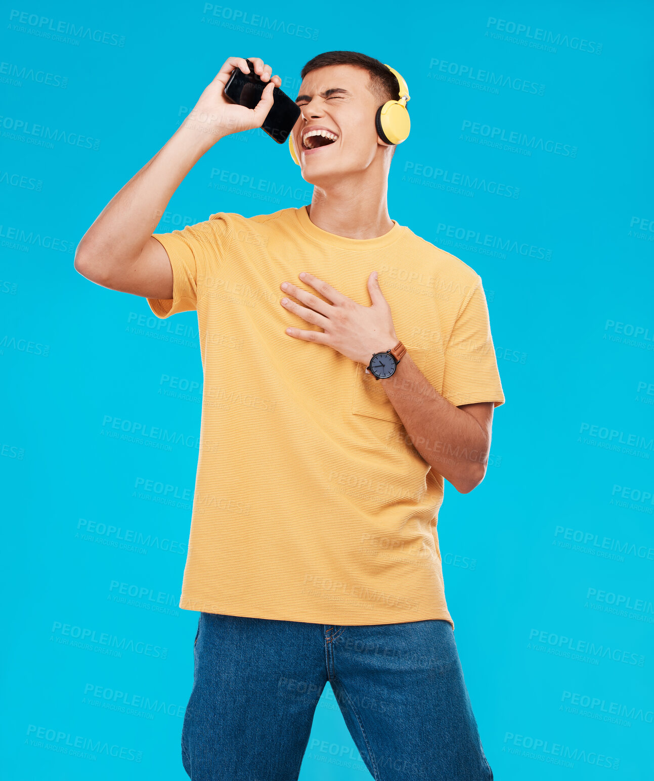 Buy stock photo Phone, headphones and man singing in studio listening to music, radio or playlist for entertainment. Smile, technology and male person streaming song or album for karaoke isolated by blue background.