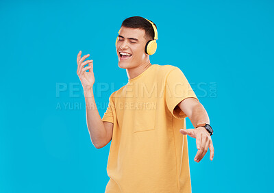 Buy stock photo Dance, headphones and young man in a studio listening to music, radio or playlist for entertainment. Smile, technology and male person moving and streaming a song or album isolated by blue background