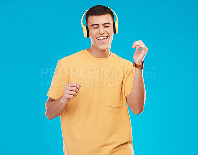 Buy stock photo Dancing, headphones and young man in a studio listening to music, radio or playlist for entertainment. Smile, technology and male person moving and streaming song or album isolated by blue background