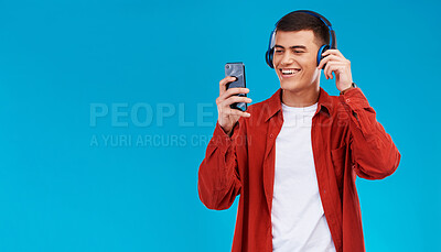 Buy stock photo Man, smile and headphones for music on phone in studio by blue background. Asian person, listening and streaming a song, radio and audio or funny podcast on smartphone, technology and sound for joy
