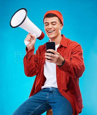 Buy stock photo Phone, megaphone and young man in a studio reading announcement or speech for a rally. Happy, cellphone and male activist or protest with bullhorn for loud communication isolated by blue background