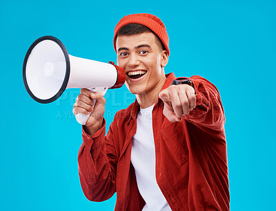 Buy stock photo Portrait, bullhorn and young man in studio pointing for an announcement or speech at a rally. Happy, smile and male activist on stool with megaphone for loud communication isolated by blue background