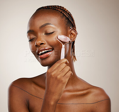 Buy stock photo Happy woman, face roller and massage for beauty, rose quartz cosmetics and aesthetic dermatology in studio on brown background. African model, crystal stone and lymphatic drainage for facial skincare