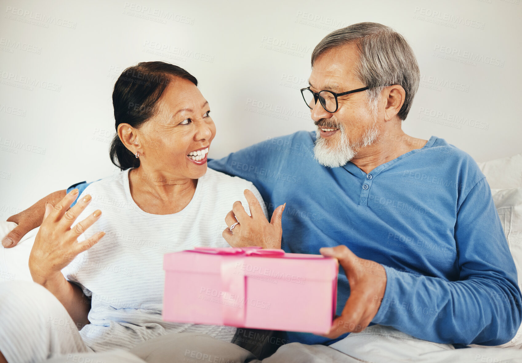 Buy stock photo Senior, man and woman with gift in bedroom for anniversary, romantic or together. Asian, elderly couple and bond by smile in happiness for celebration by surprise expression on face, embrace and love