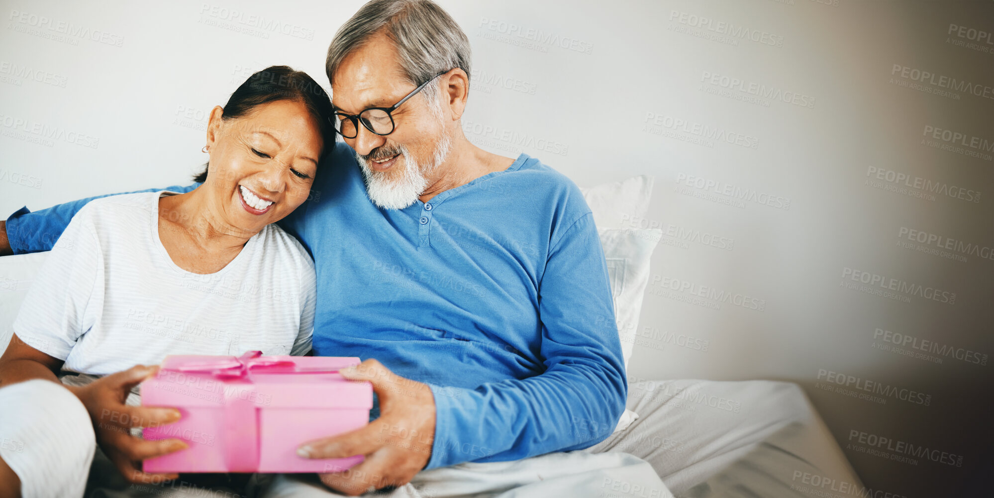 Buy stock photo Happy couple in bed, senior or hug for gift for anniversary, care or love in home, house or retirement. Giving, Asian man or excited mature woman with birthday present box for romance in bedroom