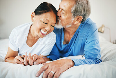 Buy stock photo Love, holding hands and senior couple on bed for bonding, kissing and relaxing together at home. Happy, care and elderly Asian man and woman in retirement embracing for connection in bedroom at house