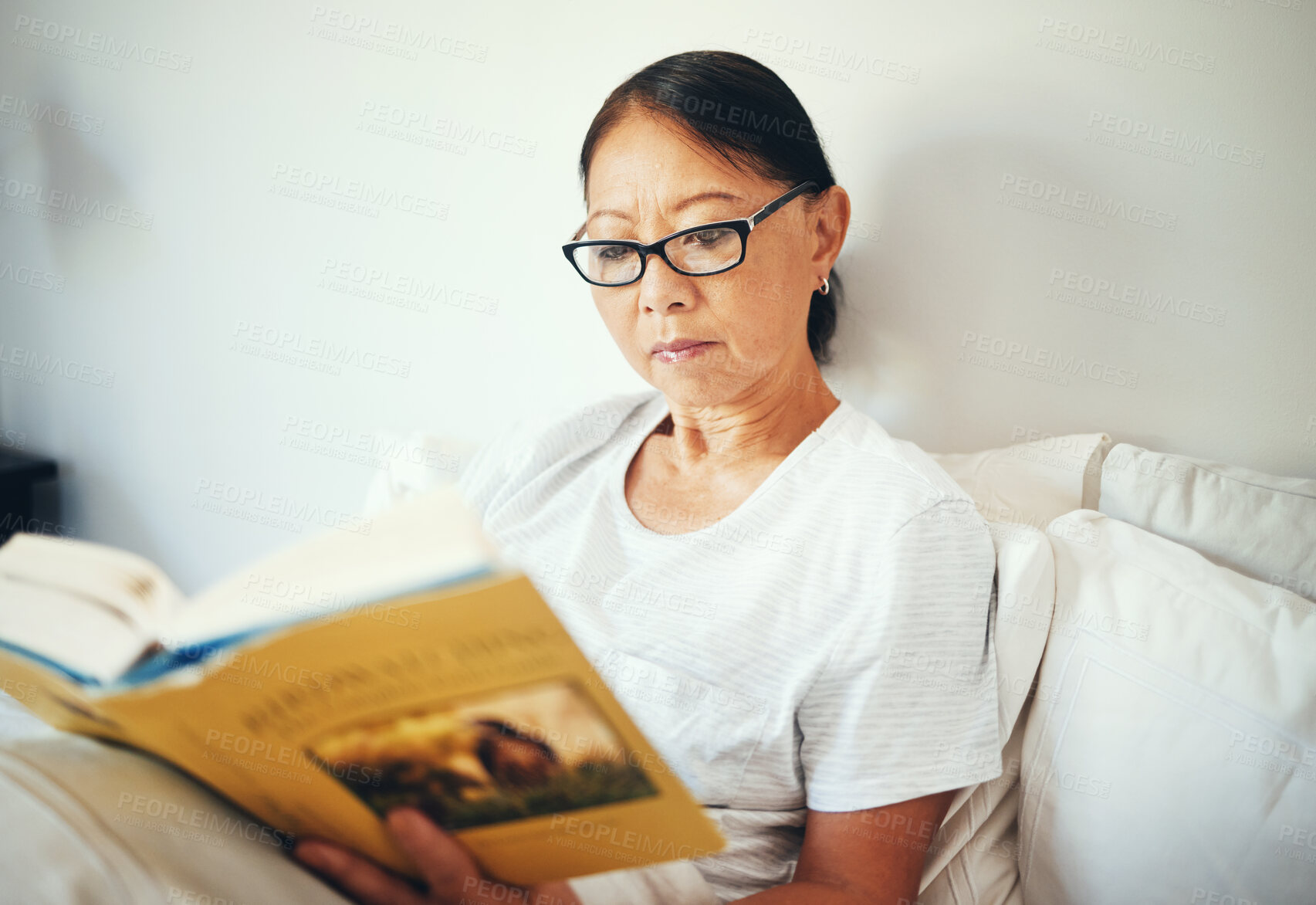 Buy stock photo Serious, woman and reading books in bedroom for story, fiction novel and knowledge at home. Mature asian person, glasses and comfortable in bed with literature for rest, hobby or relax to enjoy break