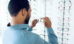 Optometry, vision and man with glasses for decision, choice and eye care option in optician store. Healthcare, ophthalmology and person in clinic to choose prescription lens, spectacles and frames