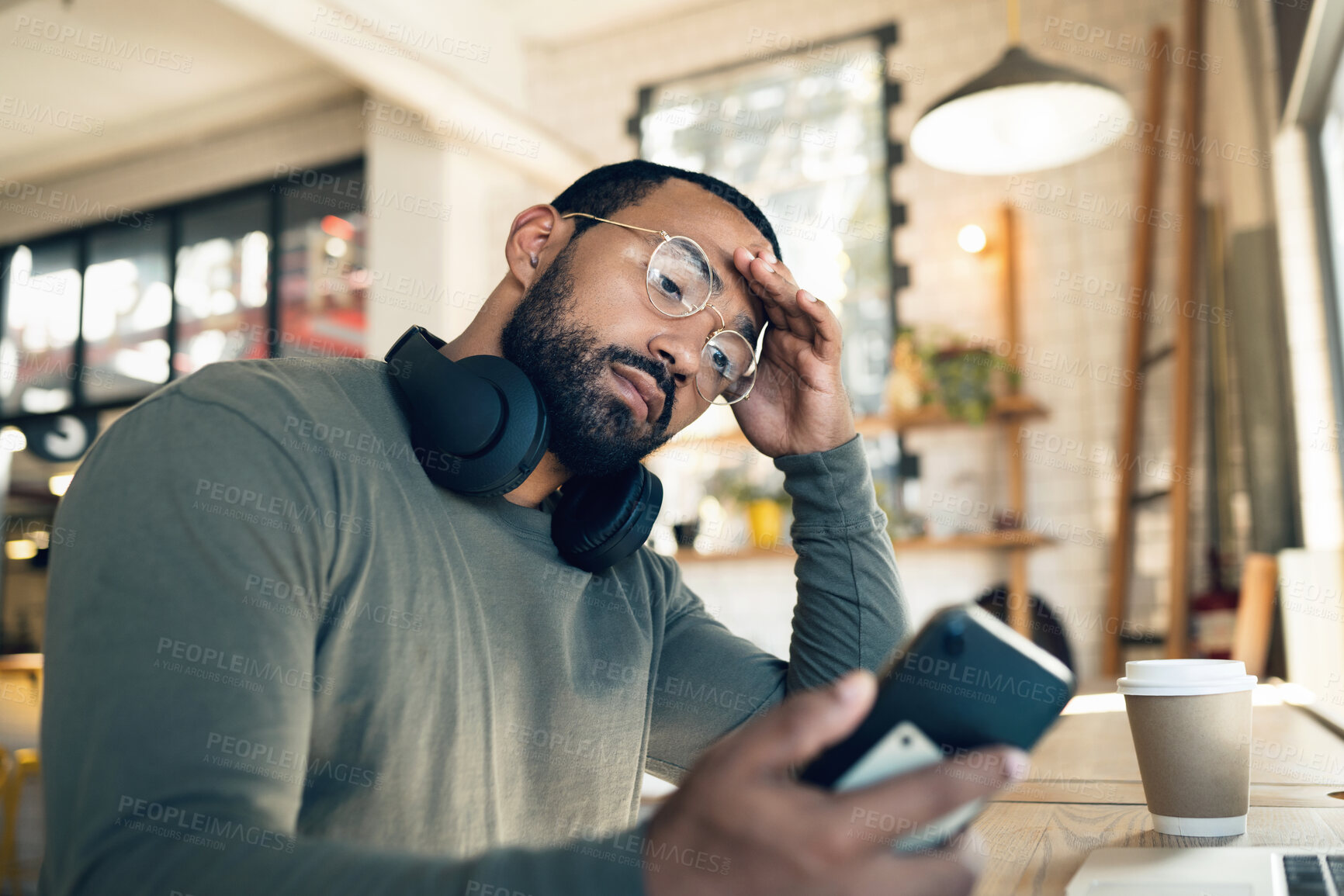 Buy stock photo Man, phone and headache in coffee shop for remote work, job search or bad news of financial fail, debt or loan. African person with stress, worry or confused reading information on his mobile at cafe