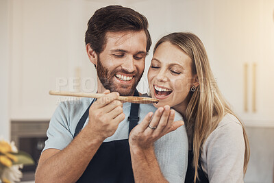 Buy stock photo Couple, cooking and taste test in kitchen with romance, support and love in their home together. Food, spoon and man feeding woman in house while preparing a delicious meal with fun and bonding