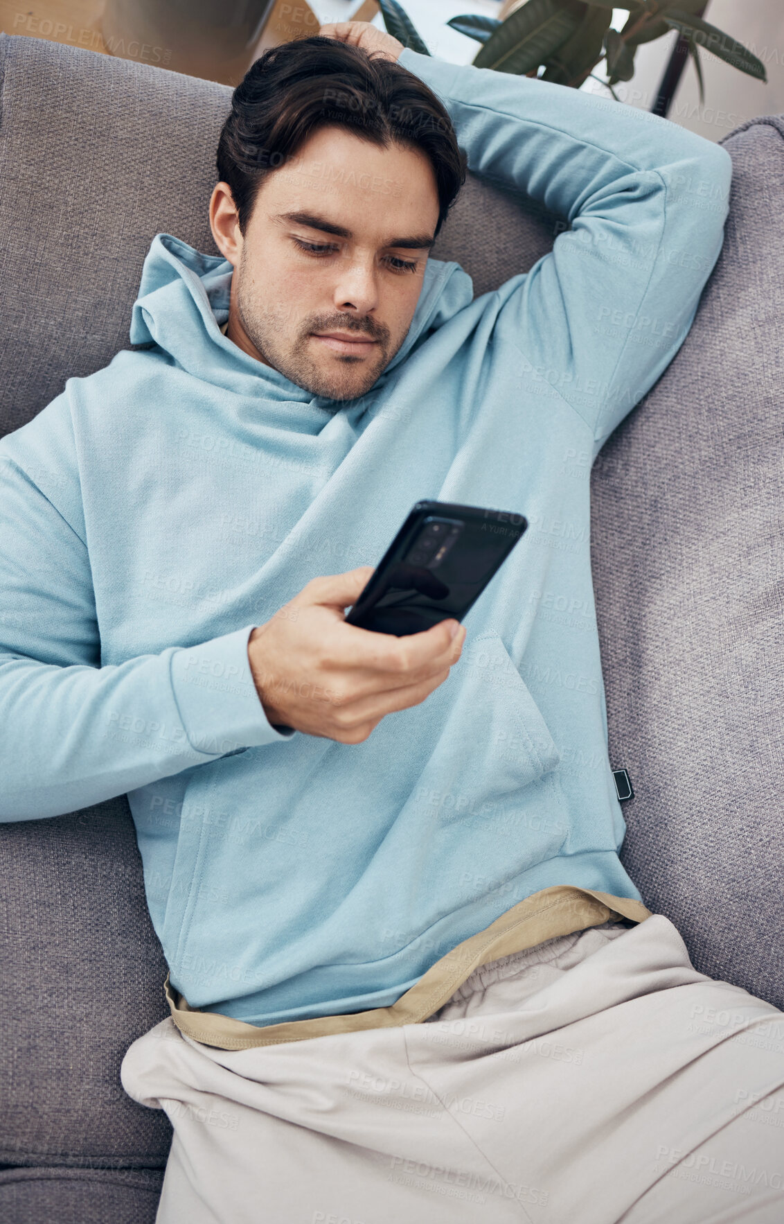 Buy stock photo Man, phone and relax on sofa for social media, communication or networking in living room at home. Male person lying on lounge couch for online chatting or texting on mobile smartphone app at house