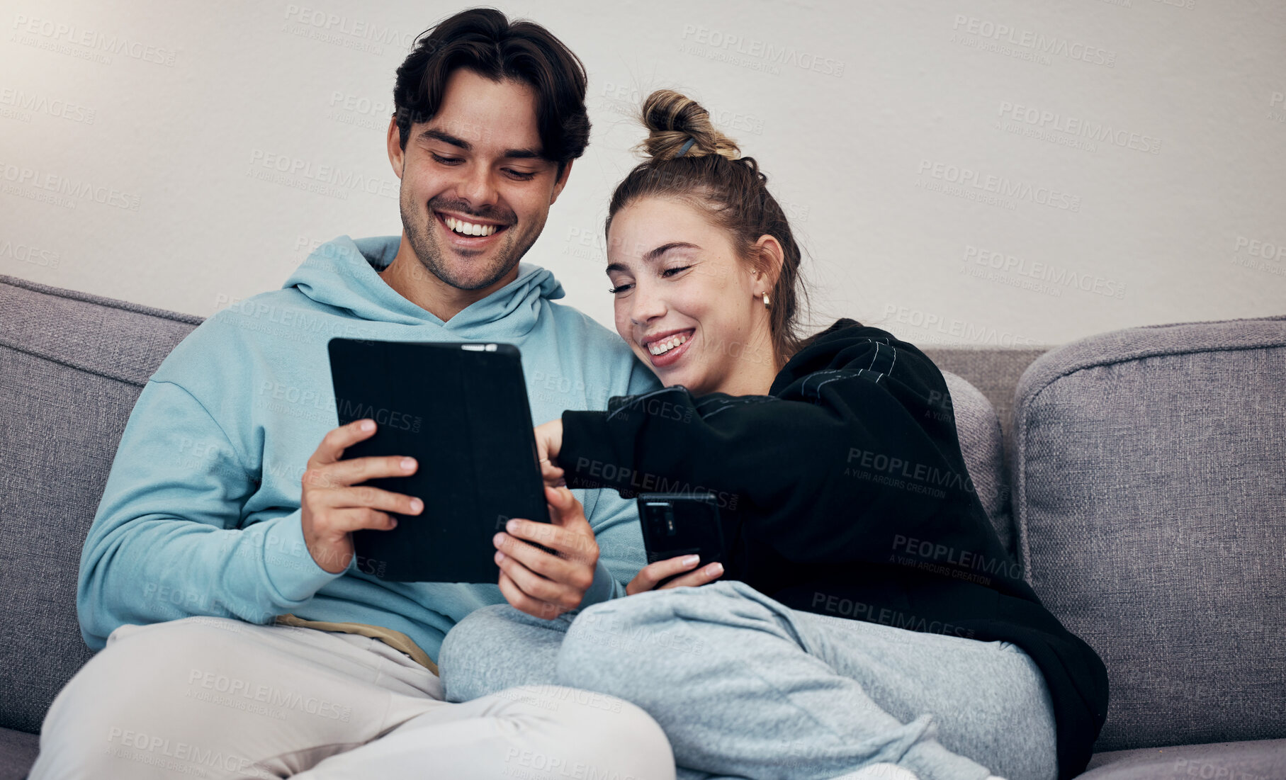 Buy stock photo Couple, phone and tablet with laugh on sofa for social media, internet scroll and funny meme with relax. People, man or woman on couch with smartphone and touchscreen for technology and web streaming