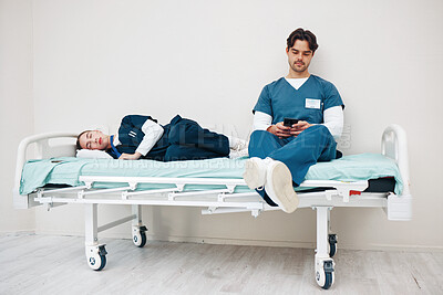 Buy stock photo Tired doctors, woman and man in hallway with phone, texting and relax on bed at hospital job. Medic team, partnership or friends with burnout, smartphone and fatigue with healthcare, clinic and rest