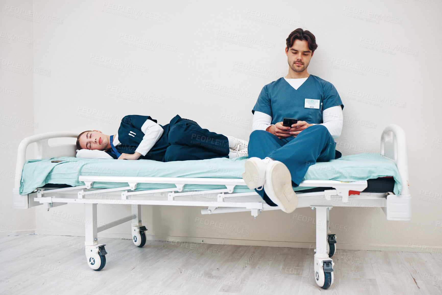 Buy stock photo Tired doctors, woman and man in hallway with phone, texting and relax on bed at hospital job. Medic team, partnership or friends with burnout, smartphone and fatigue with healthcare, clinic and rest