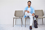 Smile, waiting and man in the office for recruitment meeting with human resources for hiring. Discussion, professional and person sitting on a chair for job interview in hallway in modern workplace.