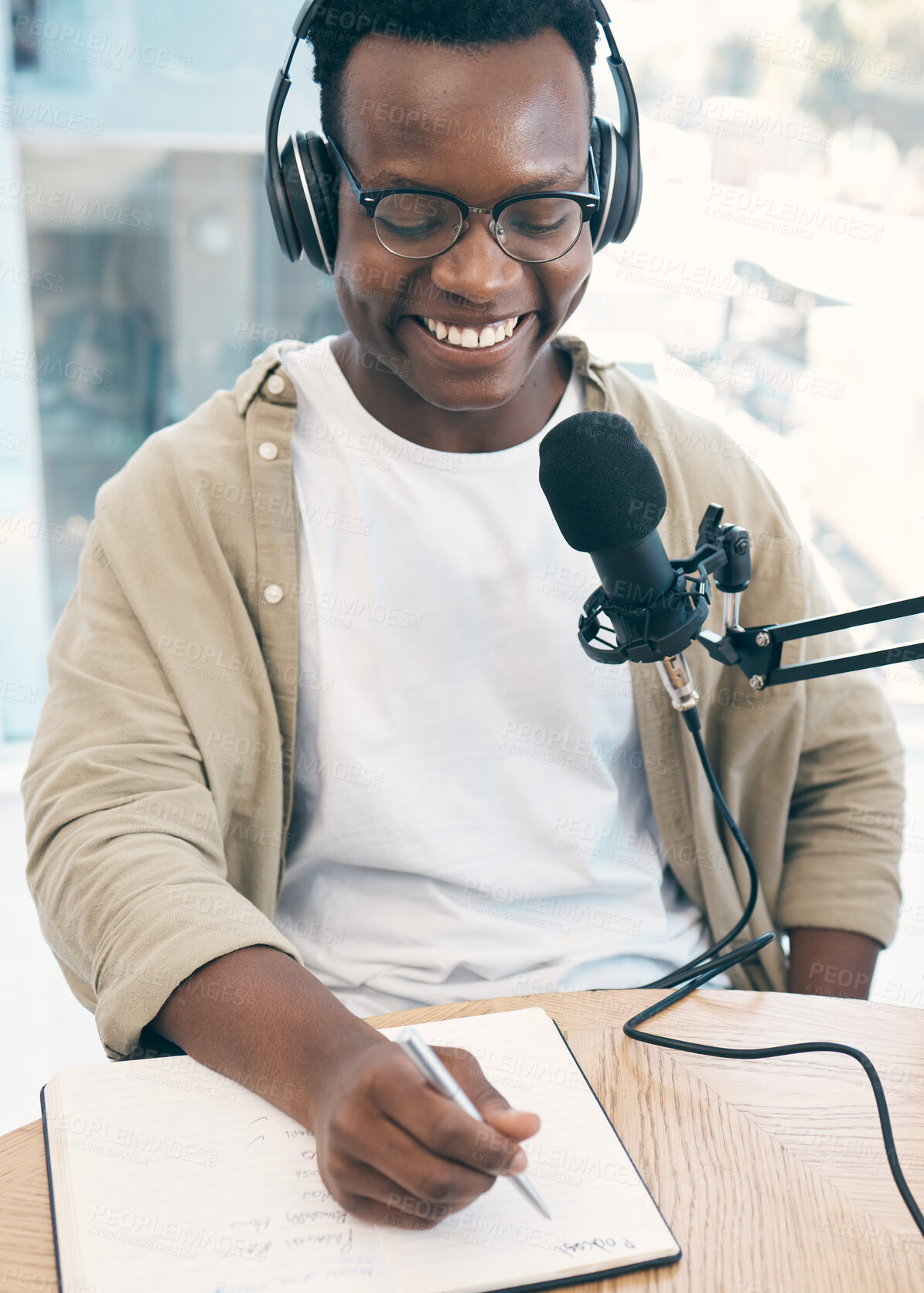 Buy stock photo Live stream, podcast or black man with notebook, microphone or headphones with news broadcasting. Smile, African person or radio presenter with tech, public relations or writing with content creator