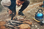 Wood, nature and man with fire on camp for kettle on an outdoor adventure, vacation or weekend trip. Stones, sticks and young male person blowing for flame or smoke in the forest on holiday in Canada
