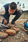 Wood, nature and man with fire on a camp on a mountain for adventure, weekend trip or vacation. Stone, sticks and young male person making a flame or spark in outdoor woods or forest for holiday.