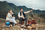 Couple, mountain and pointing in relax for camping, nature or outdoor scenery together by camp fire. Happy man and woman enjoying natural view, hiking or holiday vacation outside on trip or adventure