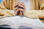 Bible, rosary and hands of woman in prayer, studying religion at desk in home with Christian faith and knowledge of God. Reading, hope and girl at table with holy book for praise, gospel and beads.