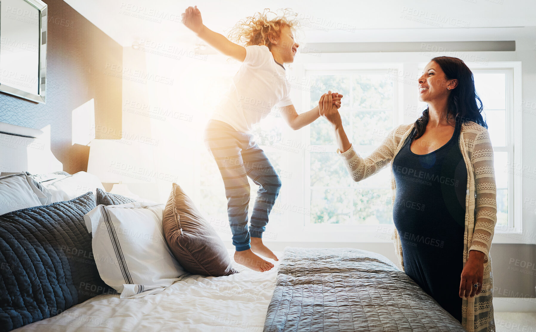 Buy stock photo Family, pregnant woman and her son jumping on the bed while in their home together. Flare, love or smile and a boy child playing in the bedroom with his happy parent for freedom, fun or bonding