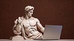 Sculpture or statue of David working on a modern laptop on a brown background