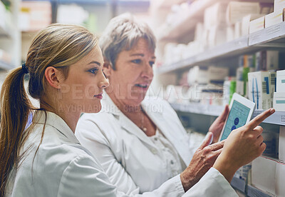 Buy stock photo Shot of two pharmacists using a digital tablet while checking stock on the shelf