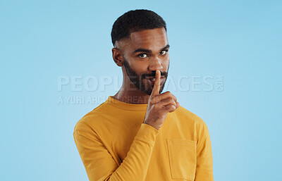 Secret, face and man with finger on lips in studio for quiet, privacy or hush news on blue background. Whisper, drama and portrait of guy model with confidential hand emoji for gossip or announcement