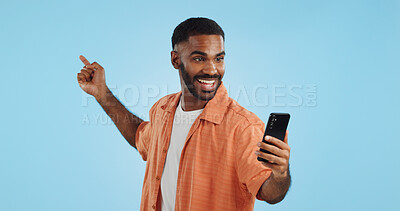 Happy, face and man with phone in hand pointing in studio for news, smartphone presentation or platform offer on blue background. Smile, portrait and male model show promo, launch or space for coming soon announcement