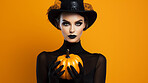 Attractive woman wearing a witch costume and holding a pumpkin on orange background