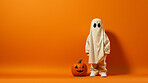 Toddler waering a ghost costume for halloween celebration on orange wall