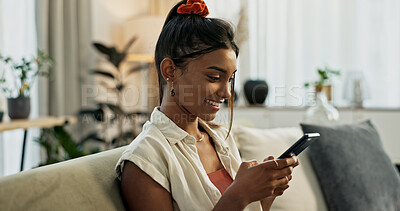 Woman, typing and smile with smartphone on sofa for social network, update multimedia subscription or chat at home. Happy indian girl, cellphone and download mobile games, reading notification or app
