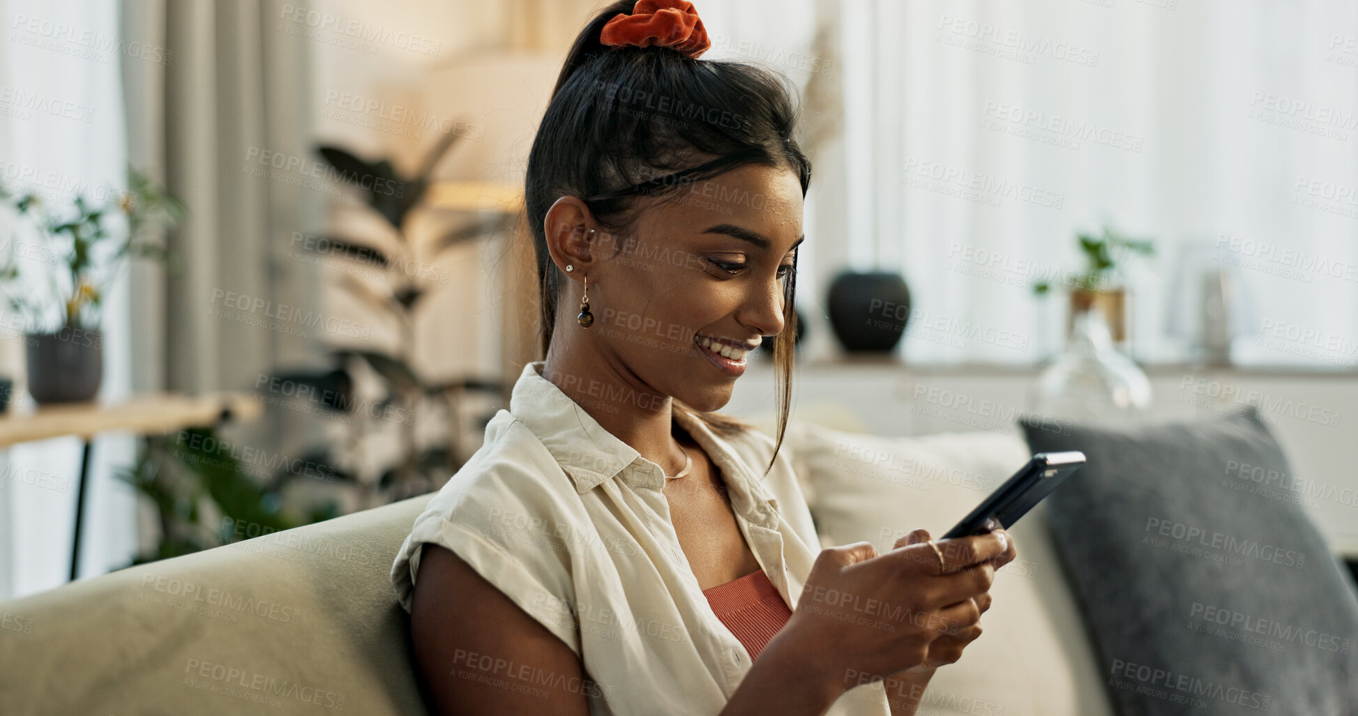 Buy stock photo Woman, typing and smile with smartphone on sofa for social network, update multimedia subscription or chat at home. Happy indian girl, cellphone and download mobile games, reading notification or app