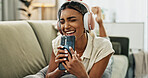 Woman, singing and phone with headphones on sofa, smile or relax for comic performance in living room. Girl, smartphone and audio streaming subscription with voice, noise or karaoke on couch in house