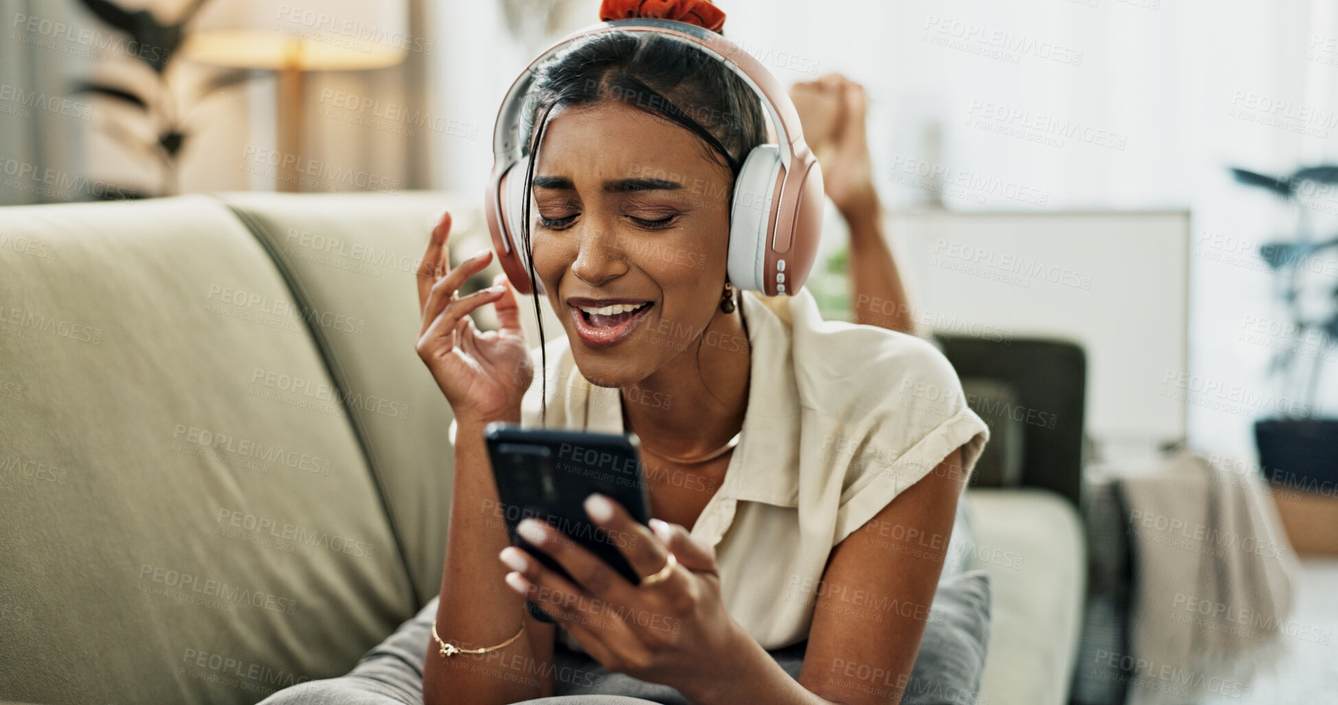 Buy stock photo Phone, music and happy woman singing on sofa in home, dance and listening to audio. Smartphone, excited Indian person on headphones for radio, sound or freedom in living room on mobile app technology