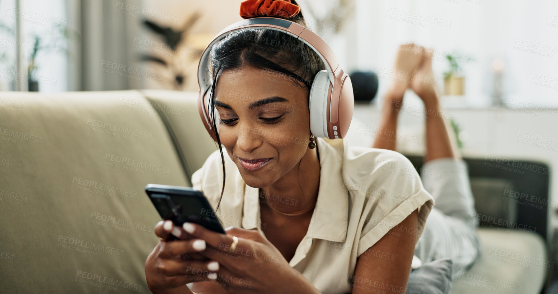 Buy stock photo Phone, music headphones and happy woman on sofa in home, listen to audio and video app to relax. Smartphone, sound and Indian person on radio or typing on social media in living room on mobile tech