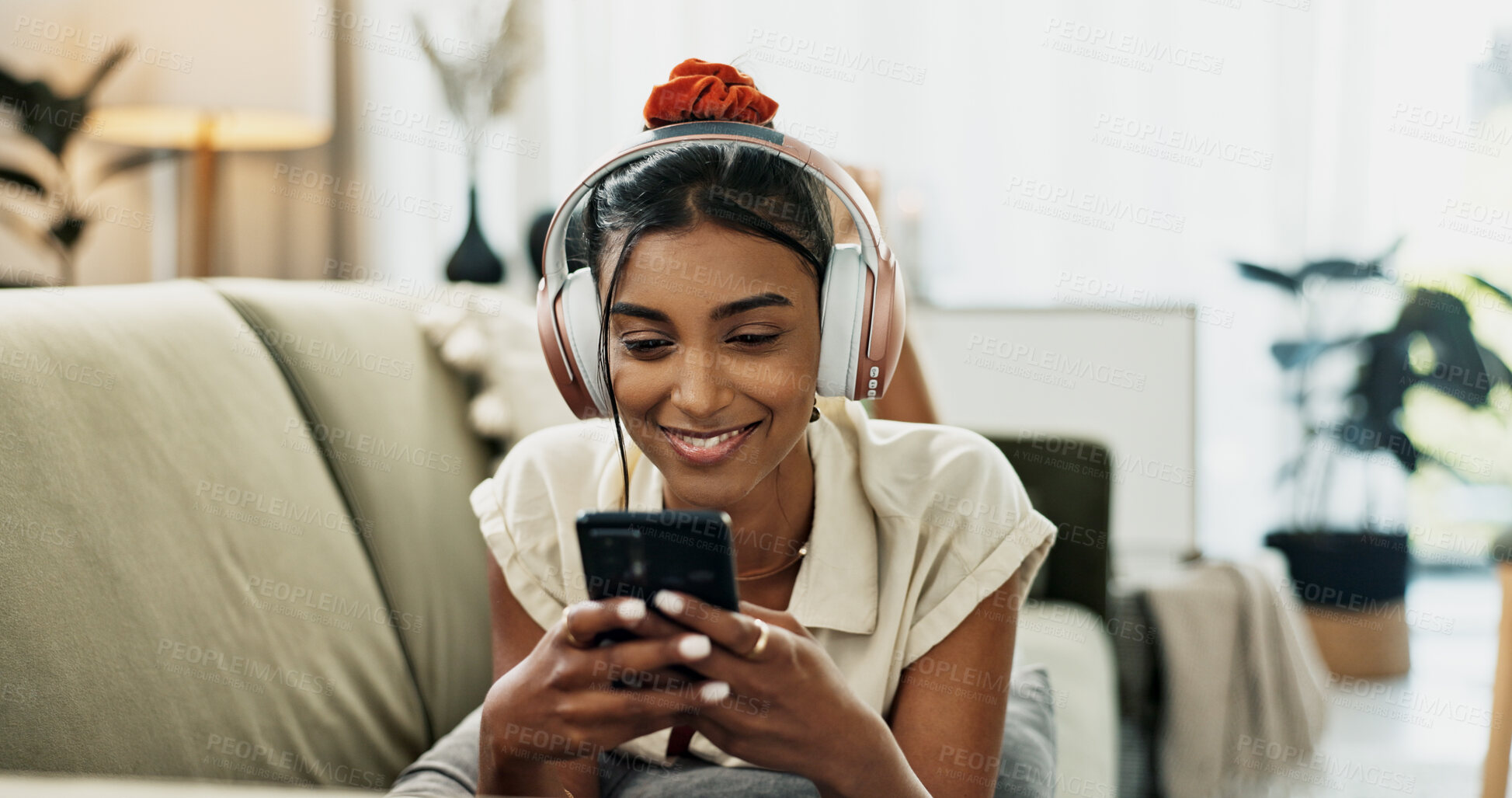 Buy stock photo Smartphone, music headphones and happy woman on sofa in home, listening to audio or video app to relax. Phone, sound and Indian person on radio or typing on social media in living room on mobile tech