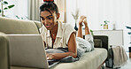 Woman, laptop and typing on sofa, relax and reading for search, thinking or e learning in home living room. Student, girl and computer on lounge couch, online course or happy for post on social media