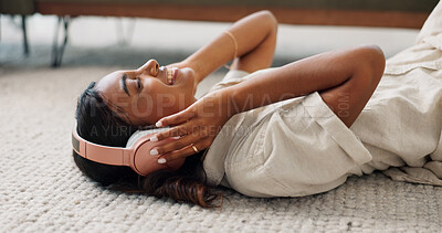 Buy stock photo Headphones, relax and young woman in the living room laying on the mat listening to music. Smile, calm and Indian female person streaming podcast, radio or playlist and chilling on the floor at home.