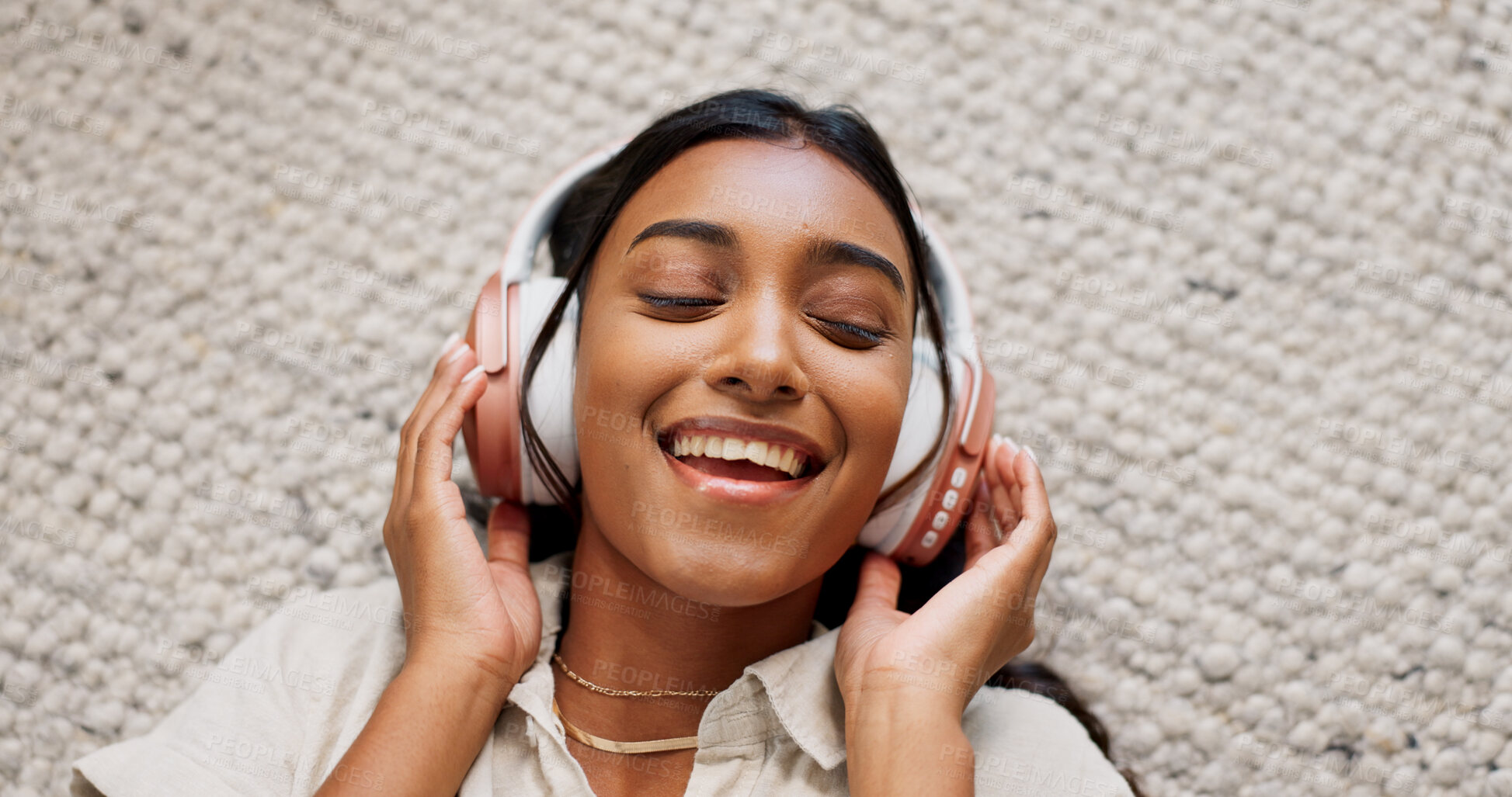 Buy stock photo Headphones, happy and young woman on the carpet on the floor listening to music or album. Smile, calm and Indian female person streaming podcast, radio or playlist and chilling in living room of home