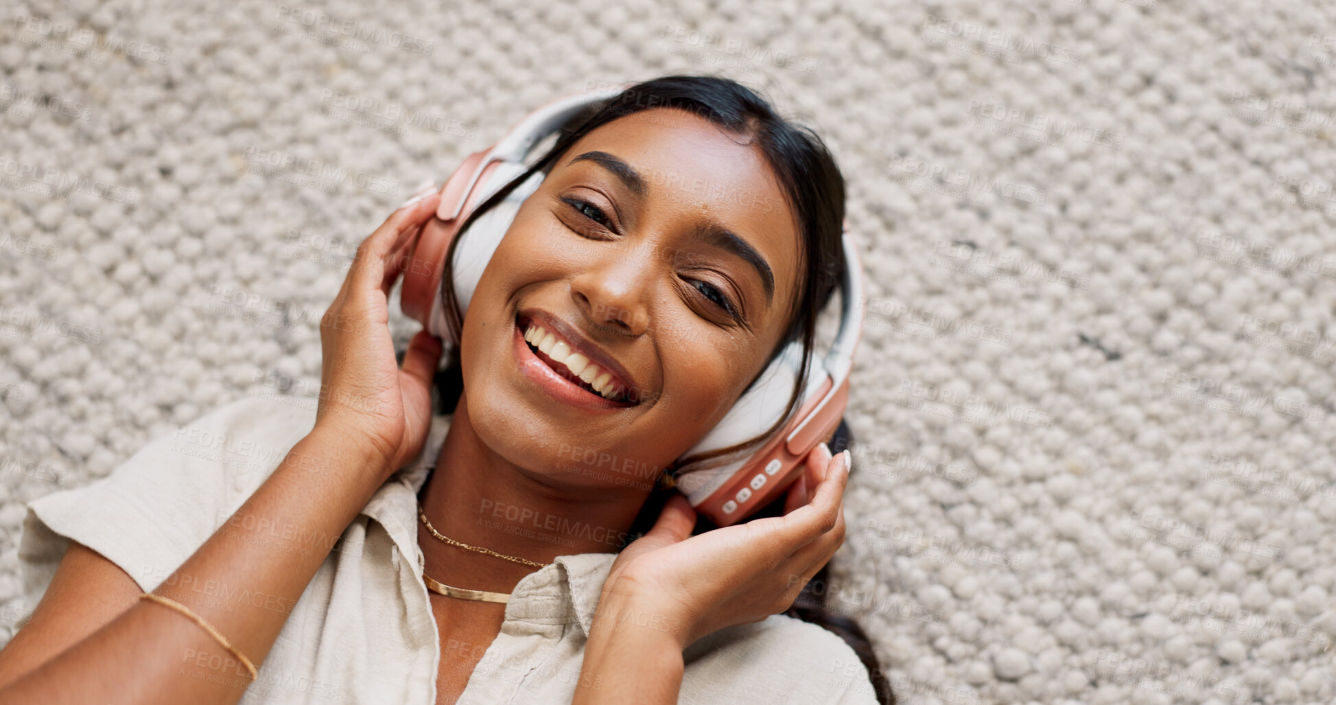 Buy stock photo Headphones, smile and portrait of woman in the living room relaxing on mat on floor. Happy, calm and Indian female person listen to podcast, radio or music and chilling in lounge at home from above.