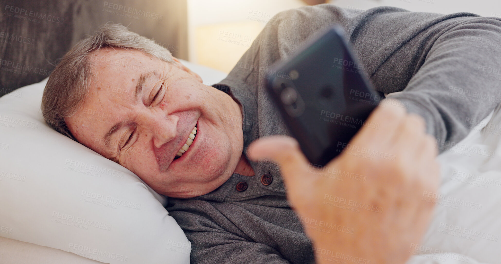 Buy stock photo Senior man, happy and reading with phone in bed or streaming funny, comedy or meme on social media. Elderly person, smile or relax with cellphone at night in bedroom with communication or online chat