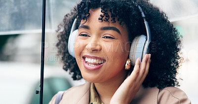 Businesswoman, headphones and smile for listening in city on commute to work with umbrella. African person, employee or manager with wireless technology for music, streaming or podcast on internet